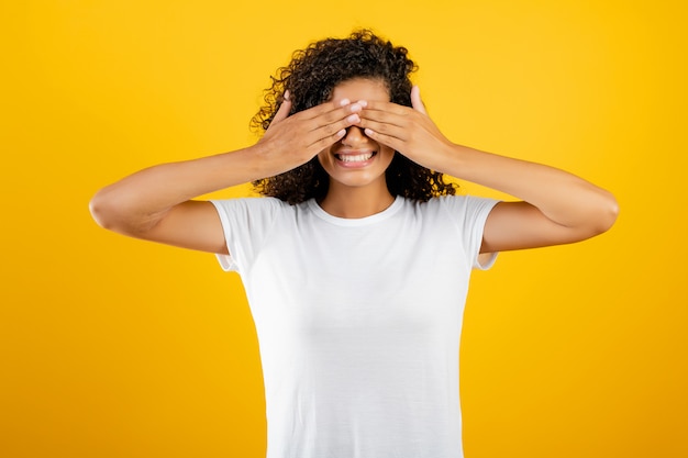 Jeune femme noire africaine couvrant ses yeux avec les mains isolées sur jaune