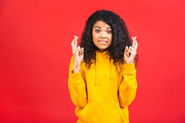 Jeune femme noire afro-américaine avec les doigts croisés isolé sur fond rouge