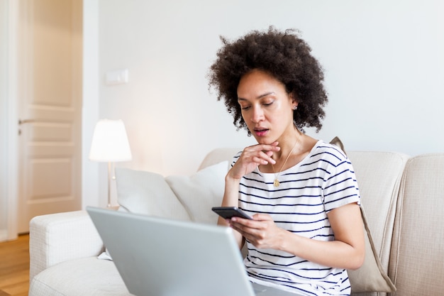 Jeune femme noire à l'aide de téléphone et ordinateur portable à la maison des SMS.