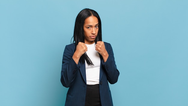 Jeune femme noire à l'air confiante, en colère, forte et agressive, les poings prêts à se battre en position de boxe. concept d'entreprise