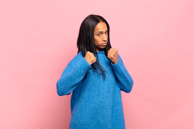 Jeune femme noire à l'air confiante, en colère, forte et agressive, avec les poings prêts à se battre en position de boxe