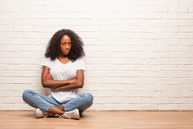 Jeune femme noire assise sur un plancher en bois très en colère et contrariée, très tendue