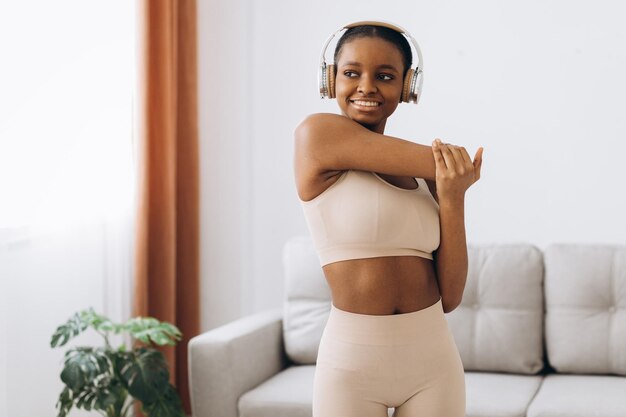 Jeune femme noire au casque écoute de la musique et fait de l'exercice à la maison dans le salon