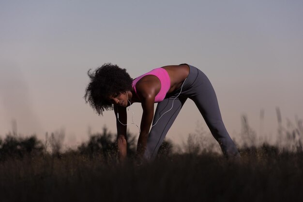 Jeune femme noire en bonne santé fait des exercices d'étirement relaxants et réchauffés après avoir fait du jogging et couru dans la nature belle soirée d'été