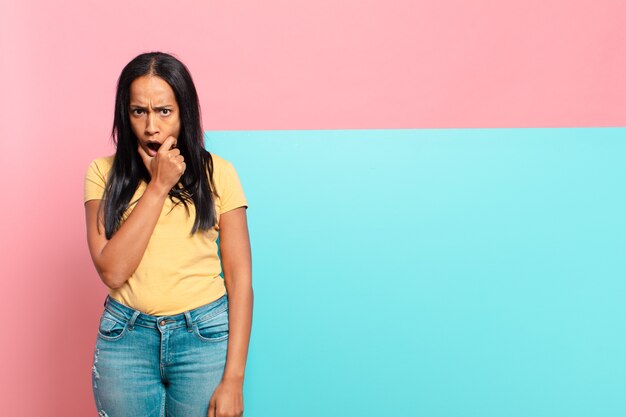 Jeune femme noire avec la bouche et les yeux grands ouverts et la main sur le menton, se sentant désagréablement choquée, disant quoi ou wow. concept d'espace de copie