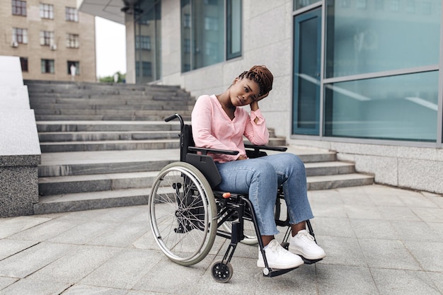 Une jeune femme noire bouleversée souffrant d'un manque d'installations adaptées aux fauteuils roulants ne peut pas entrer dans le bâtiment