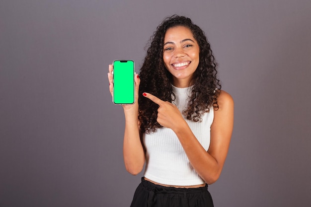 Jeune femme noire brésilienne tenant un téléphone portable et montrant une photo publicitaire à l'écran