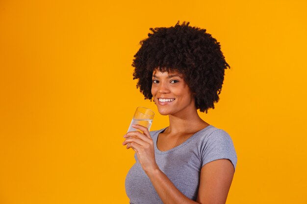 Jeune femme noire buvant de l'eau sur jaune. Jeune fille avec un verre d'eau