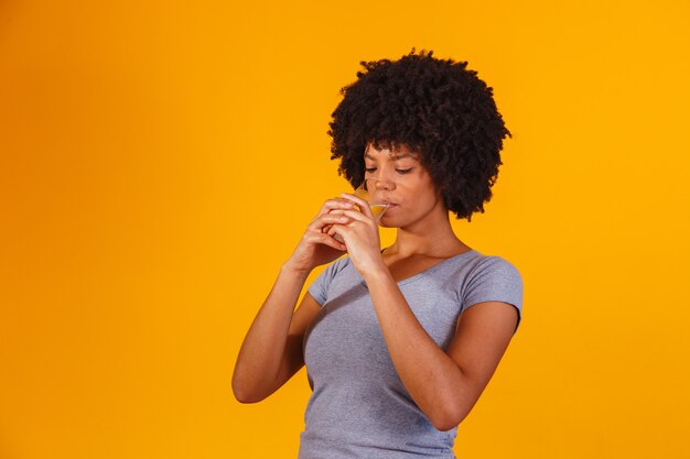 Jeune femme noire buvant de l'eau sur jaune. Jeune fille avec un verre d'eau