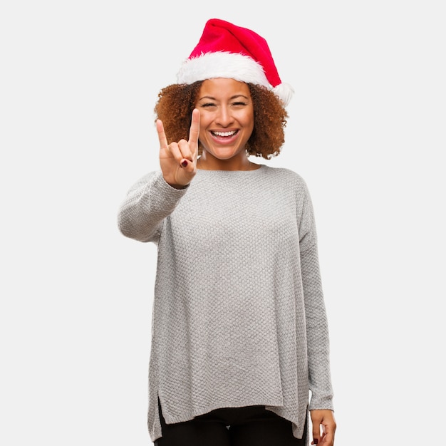 Jeune femme noire coiffée d&#39;un bonnet de Noel faisant un geste rock