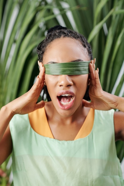 Jeune femme noire couvrant les yeux avec feuille de palmier et ouverture de la bouche