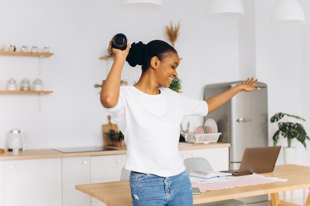 Jeune femme noire dansant dans la cuisine tenant un haut-parleur bluetooth