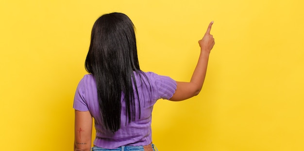 Jeune femme noire debout et pointant vers l'objet sur l'espace de copie, vue arrière