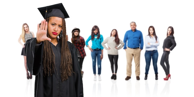 Jeune femme noire diplômée portant des tresses sérieuses et déterminées, mettant la main devant, arrêtez le geste, niez le concept