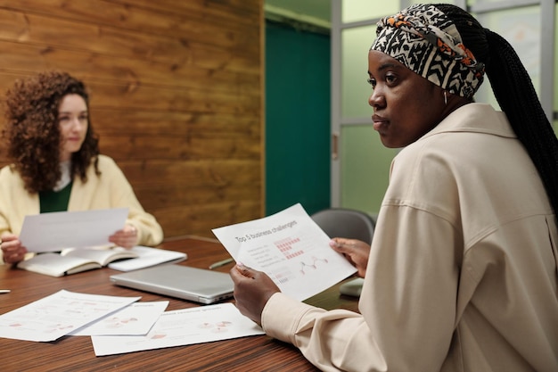 Jeune femme noire avec un document financier regardant l'un de ses collègues