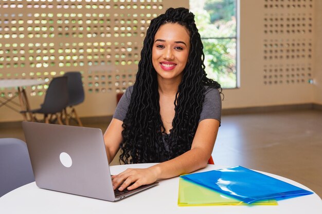 Jeune femme noire étudiante à l'université brésilienne travaillant sur ordinateur portable souriant à la caméra