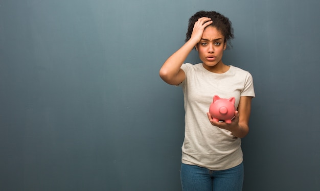 Jeune femme noire fatiguée et très endormie. Elle tient une tirelire.