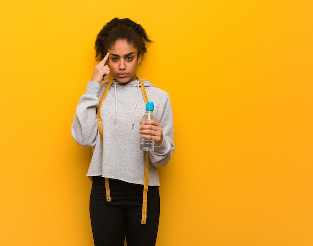 Jeune femme noire fitness faisant un geste de concentration. Tenant une bouteille d'eau.