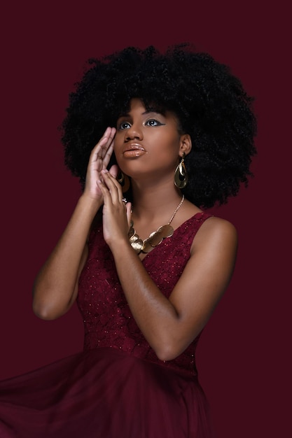 jeune femme noire avec de grands cheveux afro affiche de grandes boucles d'oreilles et un collier en or, avec une robe rouge je