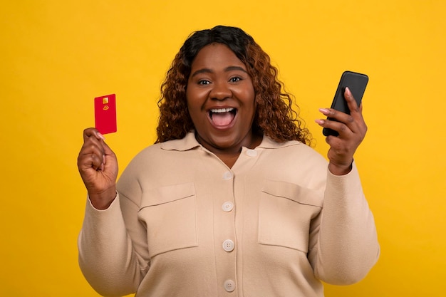 Une jeune femme noire heureuse utilisant un téléphone portable et une carte de crédit.