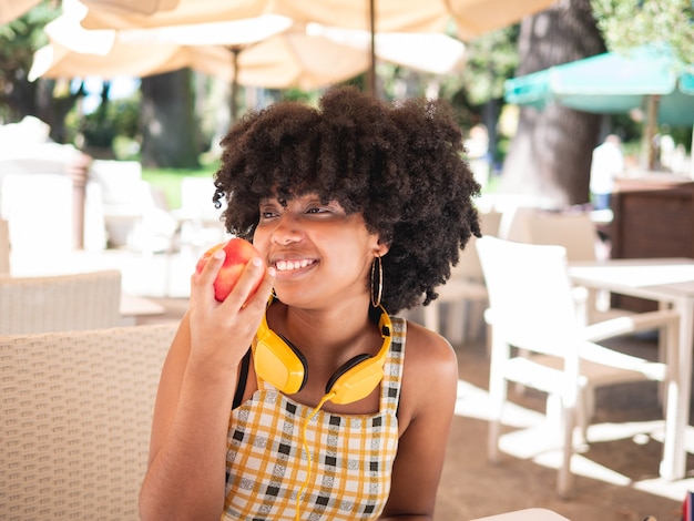 Jeune femme noire mangeant une pomme rouge fraîche alors qu'il était assis sur un café, à l'extérieur