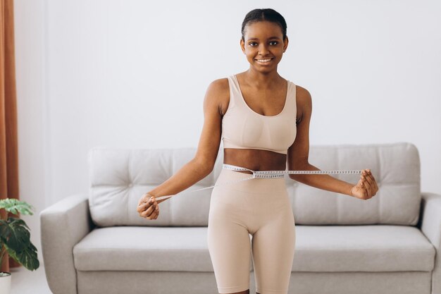 Jeune femme noire mesure sa taille sur le fond du salon Le concept de régime et de perte de poids