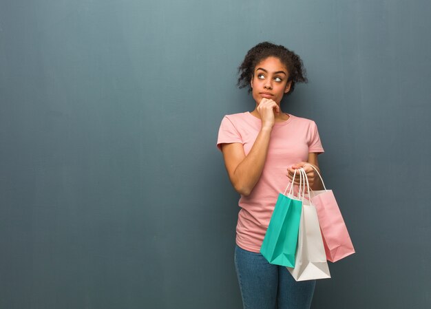 Jeune femme noire pensant à une idée. Elle tient des sacs à provisions.