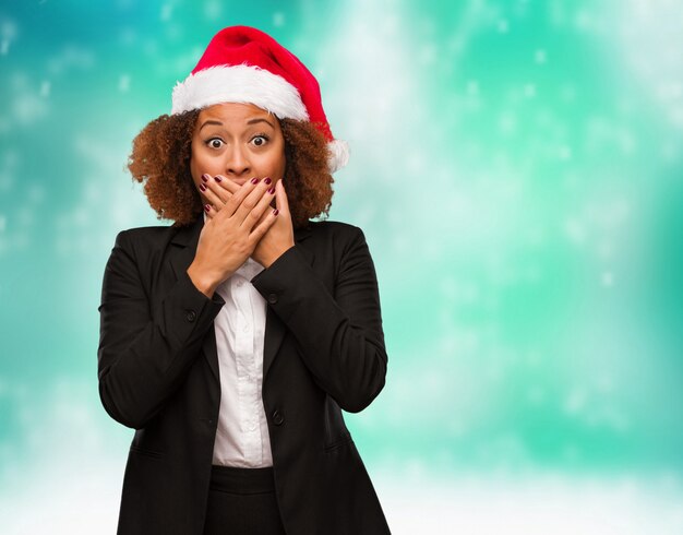 Jeune femme noire portant un bonnet de Noël chirstmas surpris et choqué