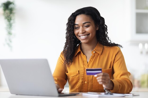 Jeune femme noire positive à l'aide d'un ordinateur portable détenant une carte de crédit