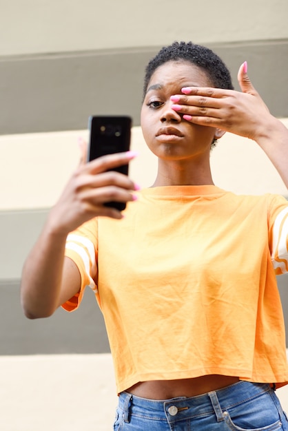 Jeune femme noire prenant selfie avec une drôle d'expression en plein air.