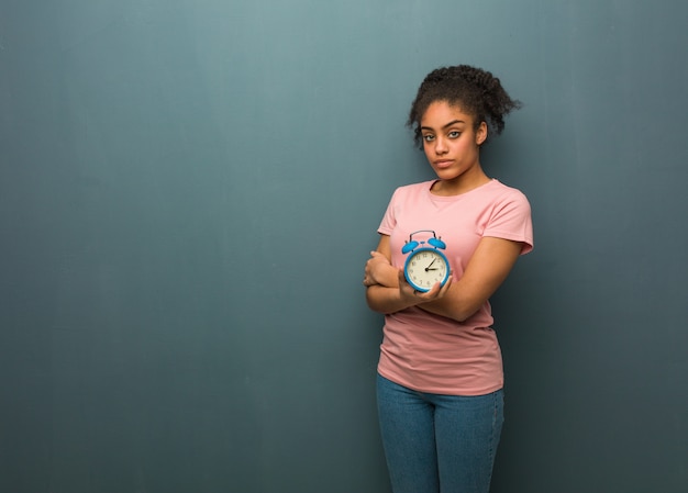 Jeune femme noire qui regarde droit devant Elle tient un réveil.