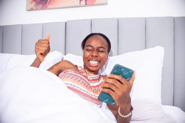 Photo une jeune femme noire qui utilise son téléphone au lit.