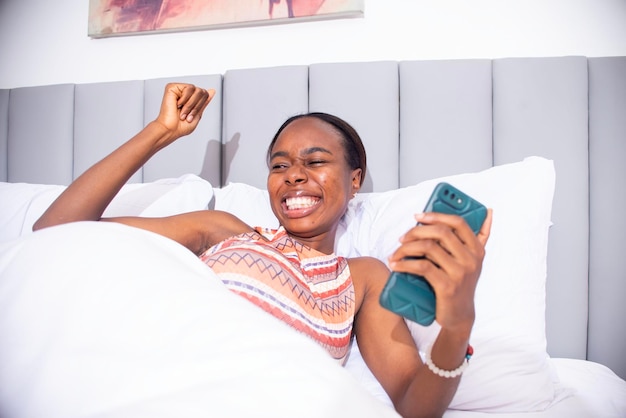 Photo une jeune femme noire qui utilise son téléphone au lit.