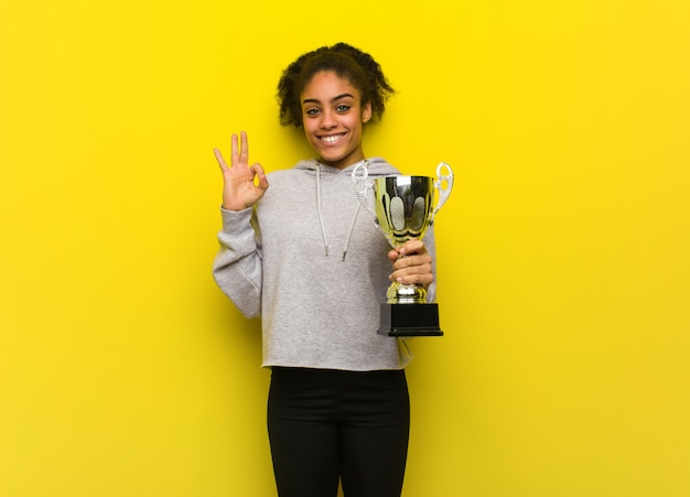 Photo jeune femme noire de remise en forme gaie et confiante faisant le geste ok. tenant un trophée.