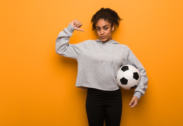 Jeune femme noire de remise en forme pointant du doigt, exemple à suivre. Tenant un ballon de football.