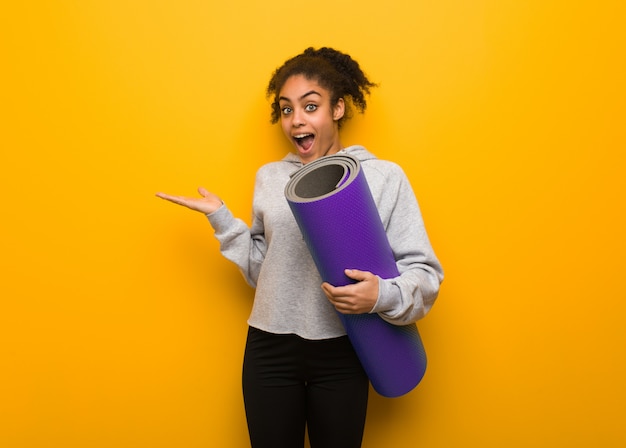 Jeune femme noire de remise en forme tenant quelque chose avec la main, tenant un tapis.