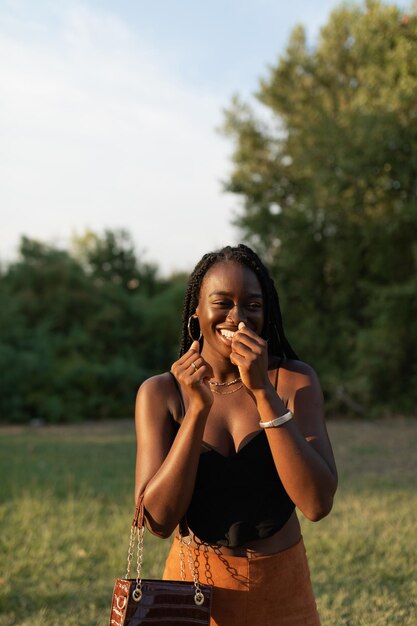 Jeune femme noire riant de façon embarrassante tout en tenant son sac à main au parc