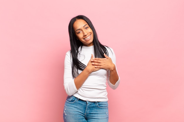 Jeune femme noire se sentant romantique, heureuse et amoureuse, souriant joyeusement et se tenant la main près du cœur