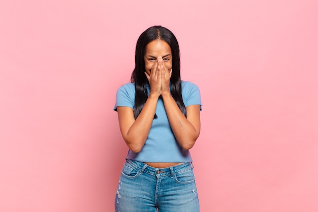 Jeune femme noire semblant heureuse, gaie, chanceuse et surprise couvrant la bouche avec les deux mains