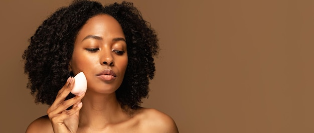 Une jeune femme noire sensuelle tenant une éponge de maquillage dans l'espace de copie.