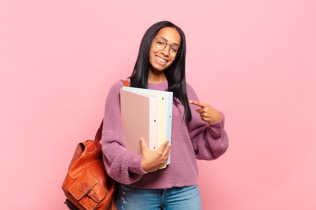 Jeune femme noire souriant joyeusement se sentant heureuse et pointant vers le côté et vers le haut montrant l'objet dans le concept d'étudiant de l'espace de copie