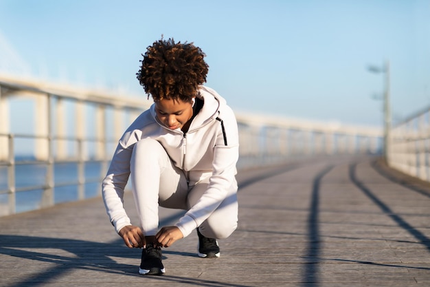 Jeune femme noire sportive attachant des lacets de chaussures se préparant pour le jogging à l'extérieur