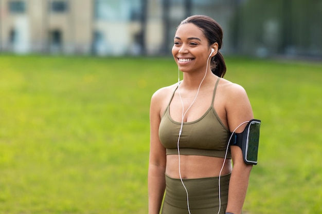 Jeune femme noire sportive avec écouteurs et téléphone portable écoutant de la musique pendant l'entraînement en plein air