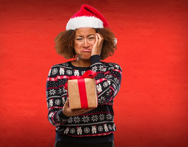 Jeune femme noire tenant un cadeau au jour de Noël désespérée et triste