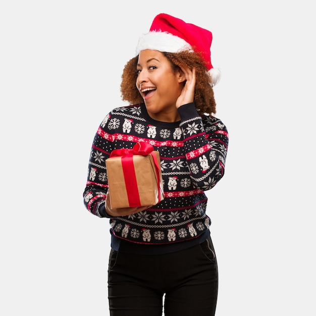 Jeune femme noire tenant un cadeau au jour de Noël, essayez d&#39;écouter un commérage