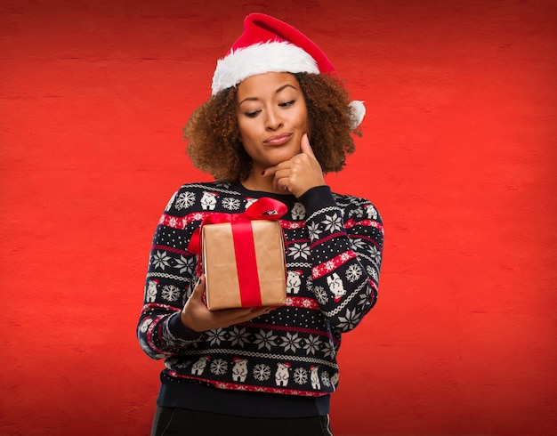 Jeune femme noire tenant un cadeau au jour de Noël, pensant à une idée