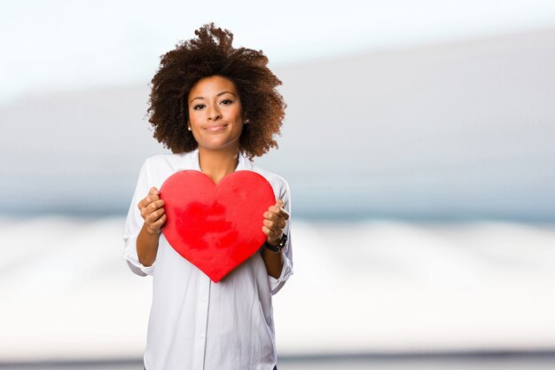 jeune femme noire tenant une forme de coeur rouge