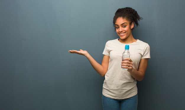 Jeune femme noire tenant quelque chose avec la main. Elle tient une bouteille d'eau.