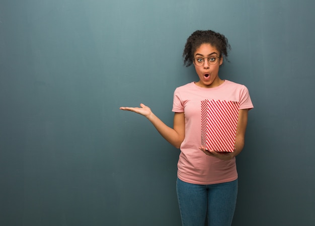 Jeune femme noire tenant quelque chose sur la main de la paume. Elle tient un seau à pop-corn.