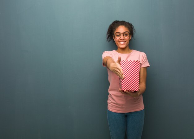 Jeune femme noire tendre la main pour saluer quelqu'un. Elle tient un seau à pop-corn.